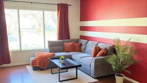 A living room with a sectional sofa, a coffee table, a potted plant, and a window with curtains. - Cozy 2BR Near Zoo, Downtown & Max Bell (Calgary)