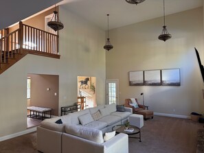 A spacious living room with a large sectional sofa, a coffee table, and a staircase leading to an upper level.