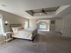 A bedroom with a bed, a nightstand, a ceiling fan, and a view of the outside.