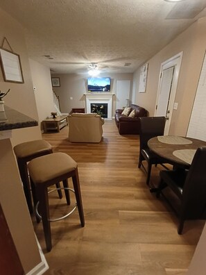 A living room with a fireplace, a television mounted above it, and a dining area with chairs and a table. - Charming 3  bedroom Home near 675/285/75   in  Ellenwood (Ellenwood)