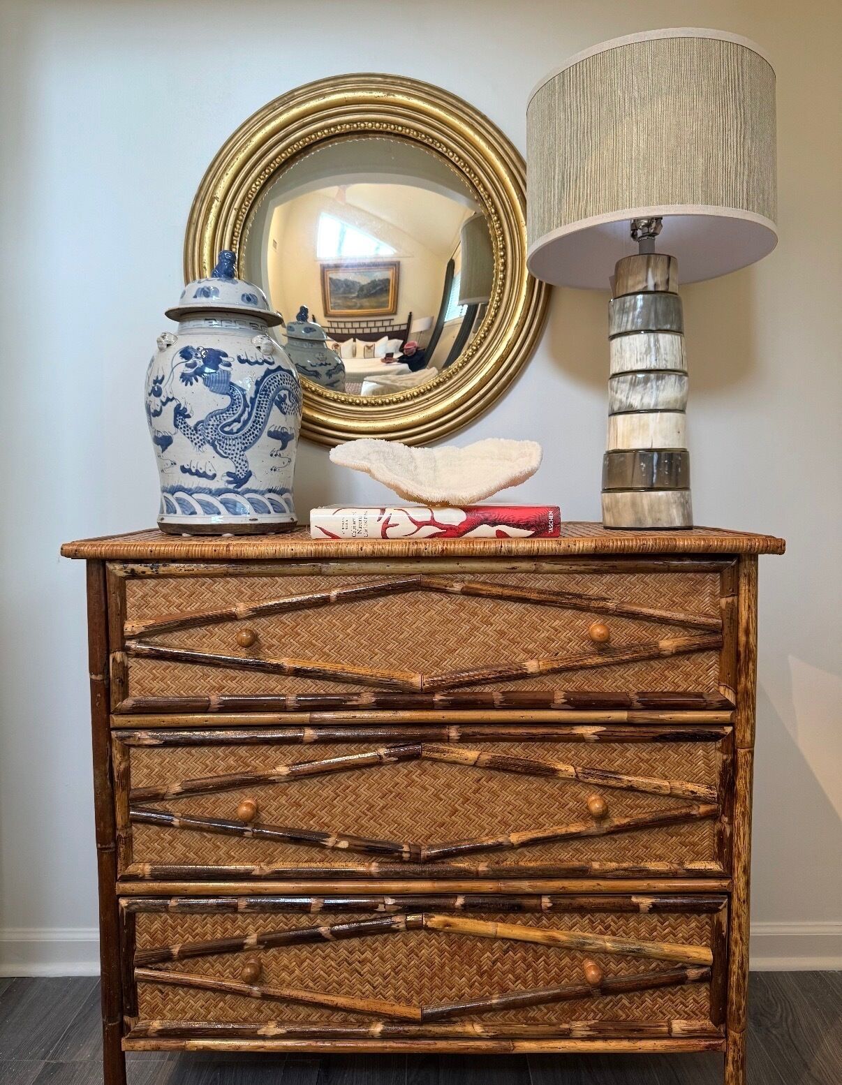 Un coffre en bois décoratif orné d’un motif tissé, un vase en céramique bleue et blanche décoré d’un motif de dragon, et une lampe avec un abat-jour cylindrique.