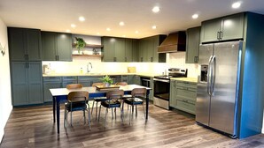 A modern kitchen with dark cabinets, a stainless steel refrigerator, and a dining area with a table and chairs. - Escape to quiet pines under star-filled skies (Pine)