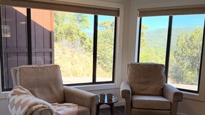 A room with two beige armchairs, a small table, and large windows with a view of trees and hills. - Escape to quiet pines under star-filled skies (Pine)
