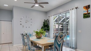 Un coin repas avec une table en bois, des chaises à rayures bleues, une plante en pot et une grande fenêtre donnant sur une piscine.