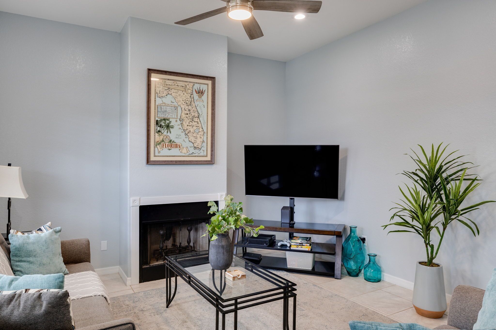A living room with a fireplace, a flat-screen TV, a ceiling fan, and a map on the wall.