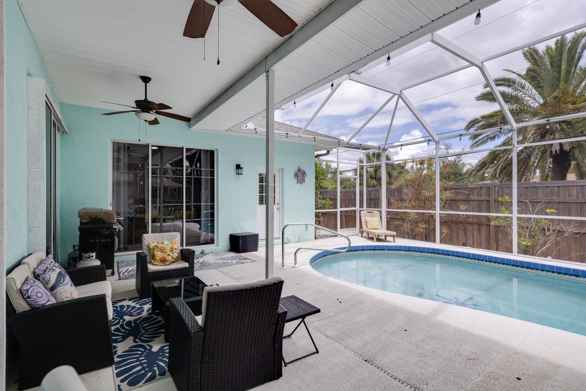 A covered outdoor area with a pool, seating, and a ceiling fan.