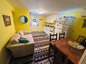 Ein kompakter Wohnbereich mit Sofa, Esstisch, Küchenzeile mit weißen Schränken und Geräten sowie einem gemusterten Teppich.