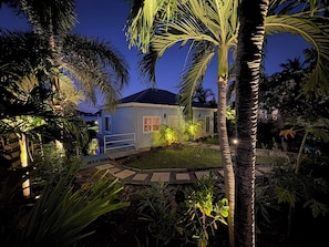 A house with a well-lit front yard, palm trees, and a pathway leading to the entrance.