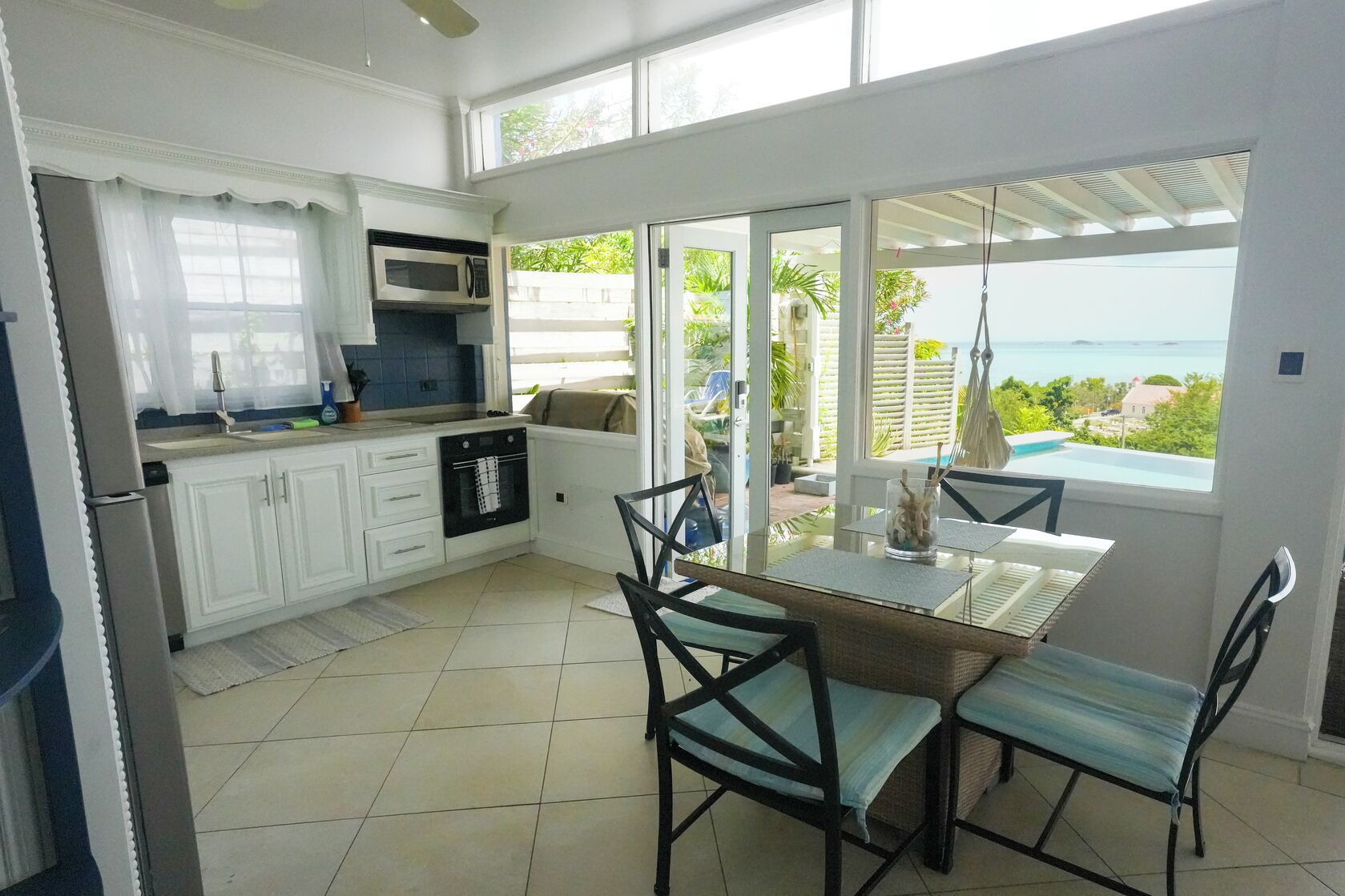 A kitchen with white cabinets, a microwave, and an oven. There is a dining table with chairs and a view of the ocean through large windows.
