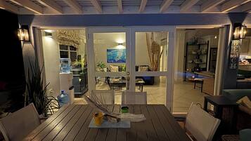 An outdoor dining area with a table and chairs, a water dispenser, and a view into the house through glass doors.