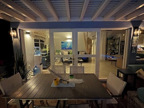 An outdoor dining area with a table and chairs, a water dispenser, and a view into the house through glass doors. - Pool views meet the sea at Starfish House (Ffryes)