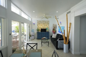 A spacious living area with a large window, a ceiling fan, a water dispenser, a television, and a blue cabinet.