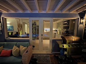 A modern kitchen with a stainless steel stove, a dining area with a blue sofa, and a visible living room with a patterned rug. - Pool views meet the sea at Starfish House (Ffryes)