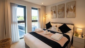 Een hotelkamer met een bed, nachtkastje, lamp en uitzicht op de natuur.