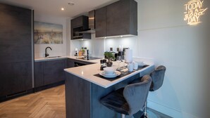 Een moderne keuken met donkere kasten, een centraal eiland, barkrukken en een neonbord.