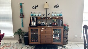 A kitchen area with a coffee station, a hanging plant, and a wall-mounted sign. - Cozy house near Kemah Boardwalk, entertainment district. (Kemah)