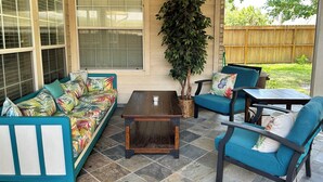 Ein überdachter Patio-Bereich mit einer Couch, Stühlen, einem Tisch und einem Topfpflanzen.