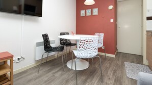 A room with a TV mounted on the wall, a round dining table with chairs, a radiator, and a door. - "Arzon" Apartment with Terrace, Shared Pool and Communal Garden (Arzon)