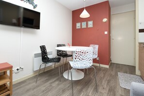 A room with a TV mounted on the wall, a round dining table with chairs, a radiator, and a door. - Apartment "Arzon" with Terrace, Shared Pool and Communal Garden (Arzon)