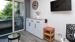 A modern room with a sliding glass door, a flat-screen TV, a decorative clock, a small table, and a chair. - "Arzon" Apartment with Terrace, Shared Pool and Communal Garden (Arzon)