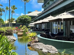 A hotel with outdoor seating, a water feature, and palm trees. - Oceanview Studio at Kauai Beach Resort #2444 (Lihue)