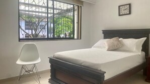 Ein Schlafzimmer mit Bett, einem Sessel, einem Fenster mit Blick und einer Wanduhr.