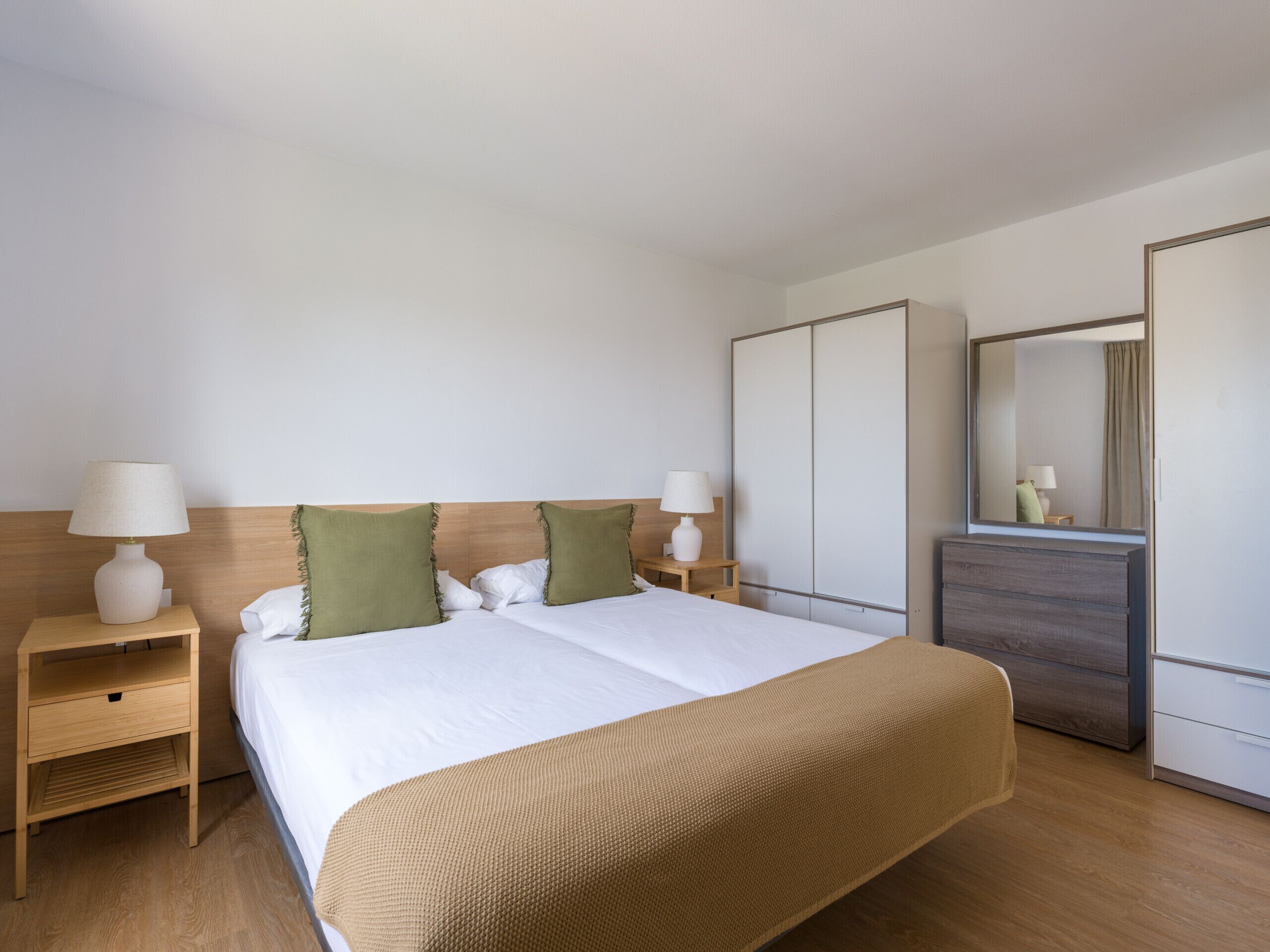 Una habitación de hotel con una cama, dos mesitas de noche, un aparador y un espejo.
