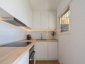 Eine kompakte Küche mit weißen Schränken, einem eingebauten Backofen, einer Kaffeemaschine und einem Fenster mit Blick.