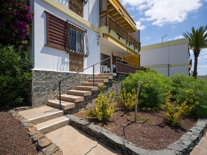 A multi-level building with a stone staircase leading to a balcony, surrounded by greenery and a palm tree. - Rocas Rojas Suites San Agustin I (Maspalomas)