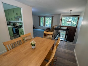 Un comedor con una mesa y sillas de madera, una cocina con armarios verdes y un balcón con vistas a árboles.