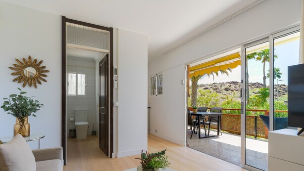 Una sala de estar moderna con una mesa de vidrio, un sofá y vistas a un balcón con mobiliario exterior.