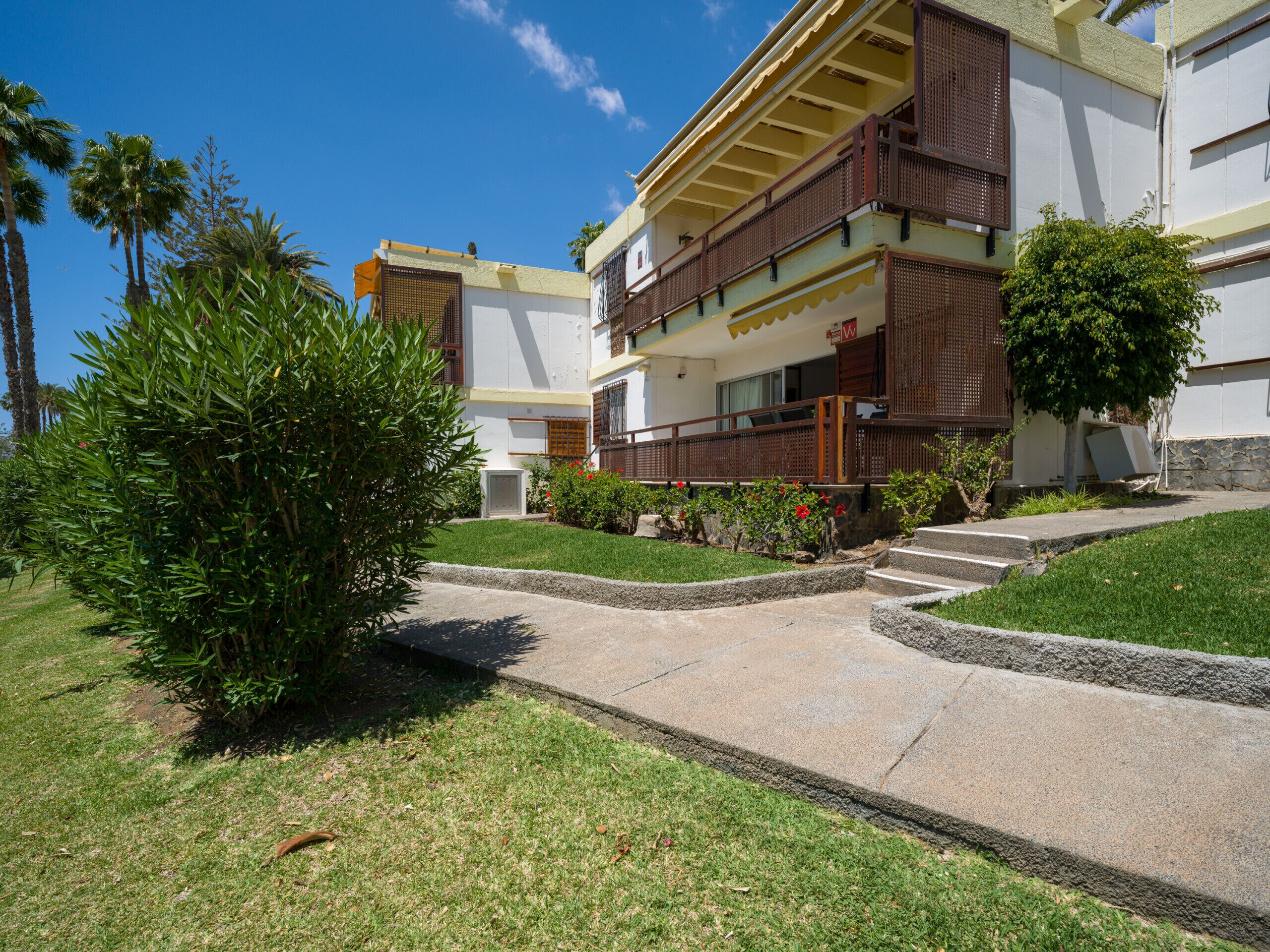 A multi-story hotel with a balcony, a well-maintained lawn, and a clear sky.