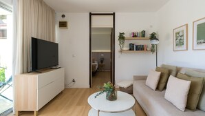 Una sala de estar moderna con televisor de pantalla plana, una mesa redonda, un sofá, una estantería y una puerta que da a otra habitación.