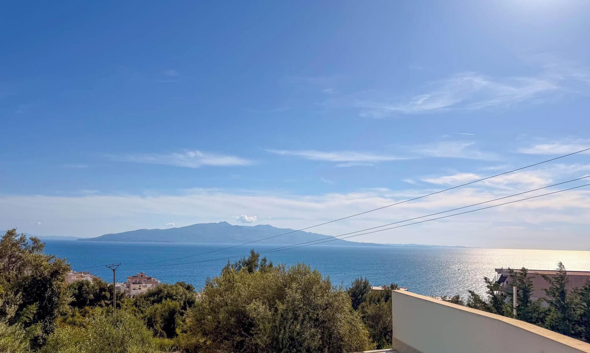 A coastal view with a clear sky, distant mountains, and a body of water.