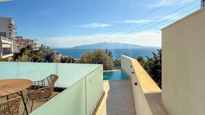 Un balcón con mesa y sillas, una piscina y vistas al mar y a las montañas.