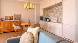 Una cocina moderna con armarios blancos, un salpicadero de mármol y un comedor con mesa y sillas de madera.