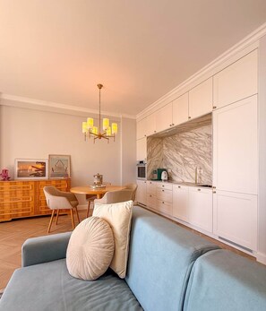 A modern kitchen with white cabinets, a marble backsplash, and a dining area with a wooden table and chairs. - Marlena - Corfu View Residence (Sarandë)