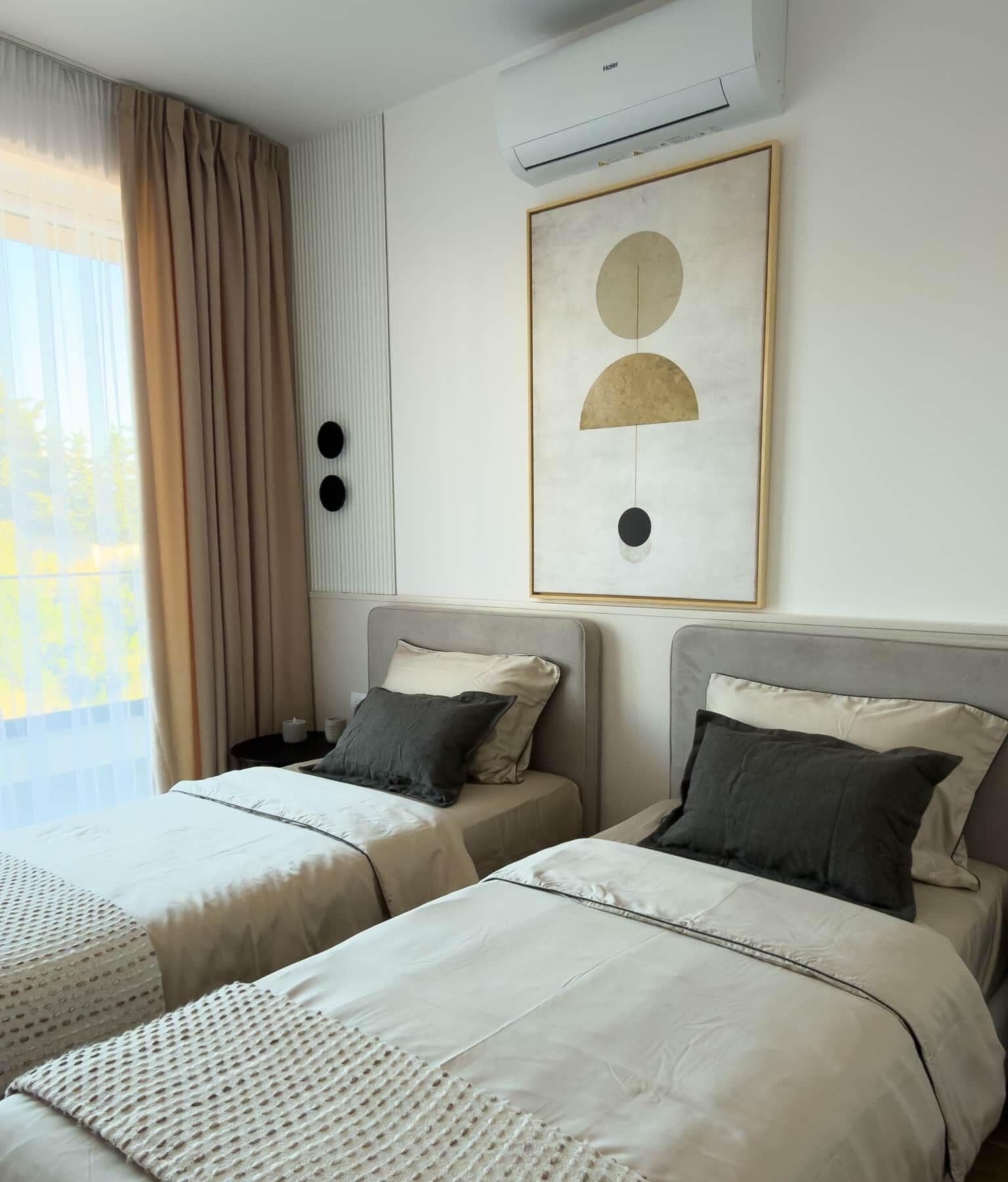 A hotel room with two beds, an air conditioner, a framed abstract artwork, and a window with curtains.