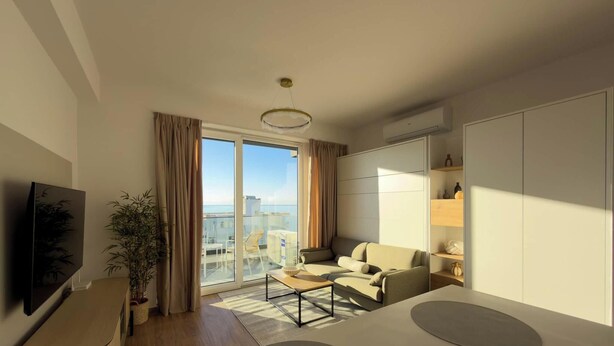 Ein modernes Wohnzimmer mit Sofa, Couchtisch und Fernseher. Ein großes Fenster mit Vorhängen, eine Pflanze und Blick auf die Stadt.