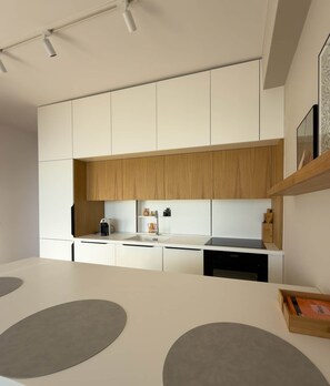 A modern kitchen with white cabinetry, a wooden accent panel, and a central island with a gray countertop. - Stelvio - Sea Residence (Sarandë)