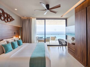 Ein Hotelzimmer mit Bett, Deckenventilator, großem Fenster mit Meerblick und Balkon mit Stühlen.