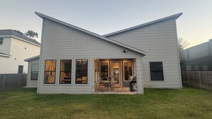 A modern two-story house with a large front porch, a dining area with a table and chairs, and a visible garage. - House in Conroe (Conroe)