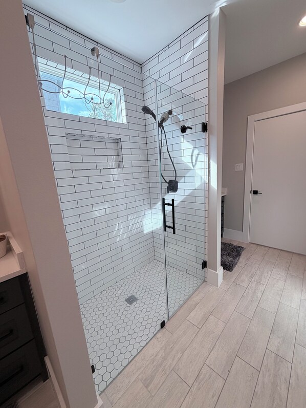 A modern bathroom with white subway tiles, a glass shower enclosure, and a wooden floor. - House in Conroe (Conroe)