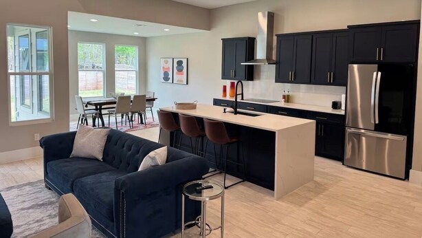 A modern kitchen with dark cabinets, a stainless steel refrigerator, and a central island. - House in Conroe (Conroe)