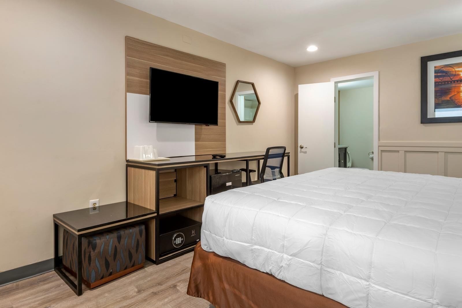 A hotel room with a bed, a desk, a chair, a TV, a mirror, and a door.