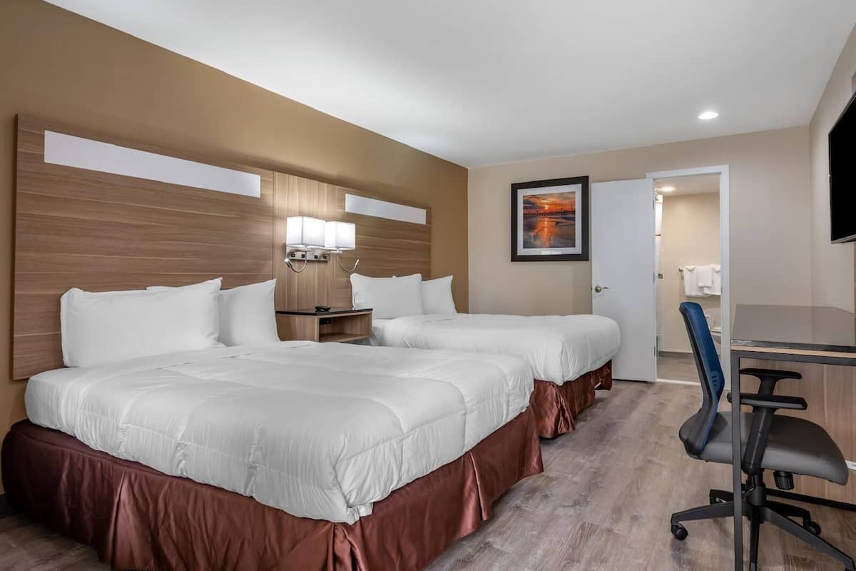 Une chambre d’hôtel avec deux lits, un bureau, une chaise, une télévision et une salle de bain visible à travers une porte ouverte.
