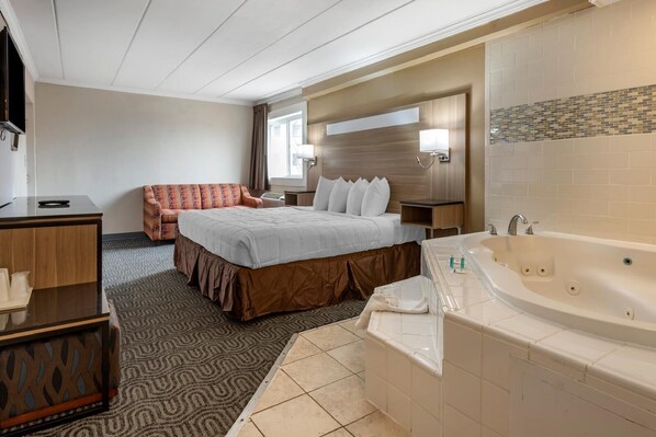 Habitación de hotel con cama, sofá, escritorio, una bañera grande y un espejo.