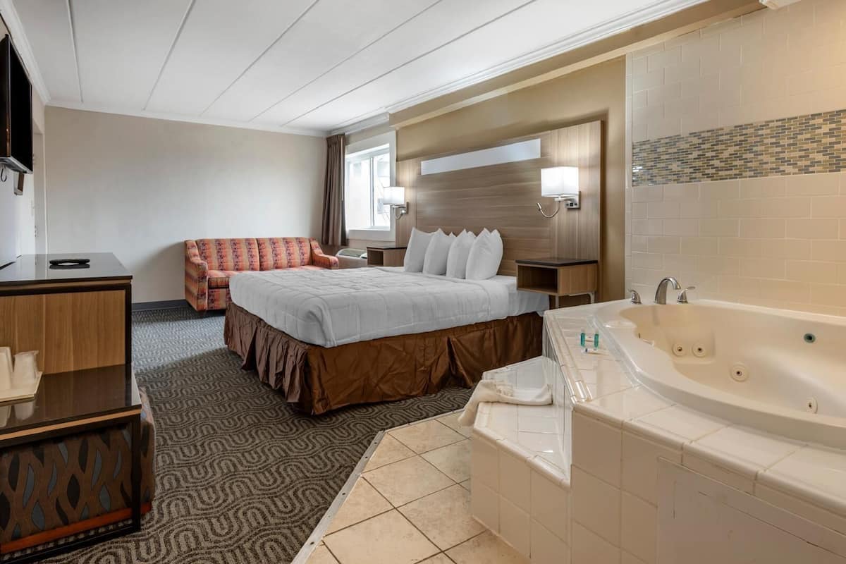 Une chambre d’hôtel comprenant un lit, un canapé, un bureau, une salle de bain avec baignoire et un grand miroir.
