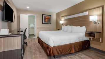 Una habitación de hotel con una cama, un escritorio, un televisor y un cuadro en la pared.