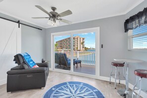 Ein Zimmer mit Deckenventilator, einer Schiebetür zum Balkon, einer schwarzen Couch, zwei Barhocker und einem Teppich mit Kompassmuster.